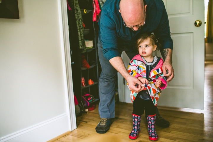 father putting raincoat on daughter