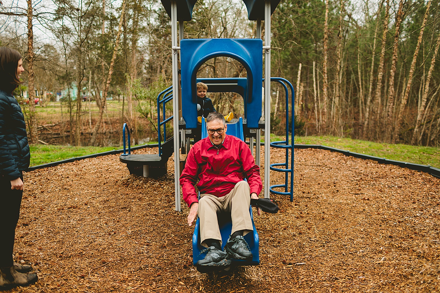 Grandpa using the slide at park while playing with grandson
