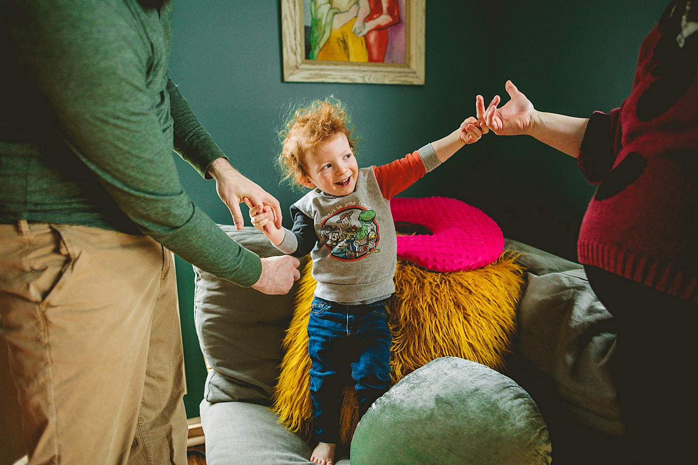 Toddler jumping on chair while parents hold his hands