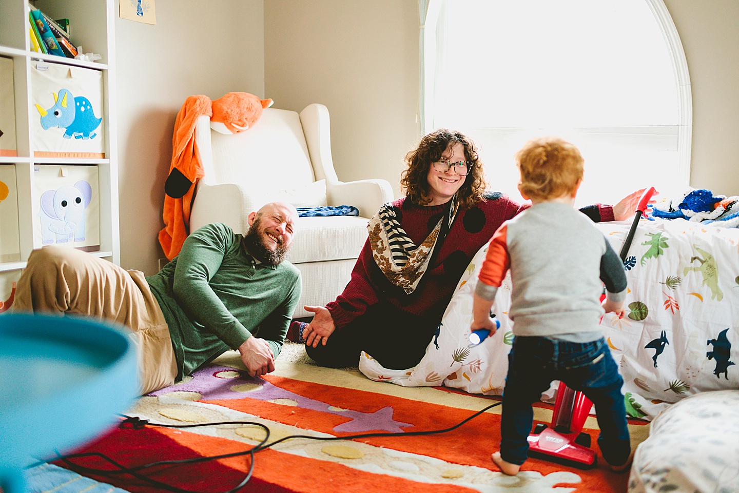 Parents smiling at toddler as he cleans room