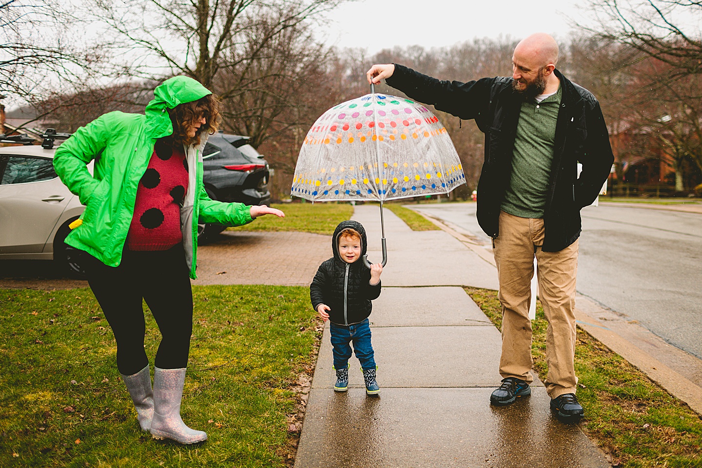 Parents taking a rainy day walk with toddler down the street