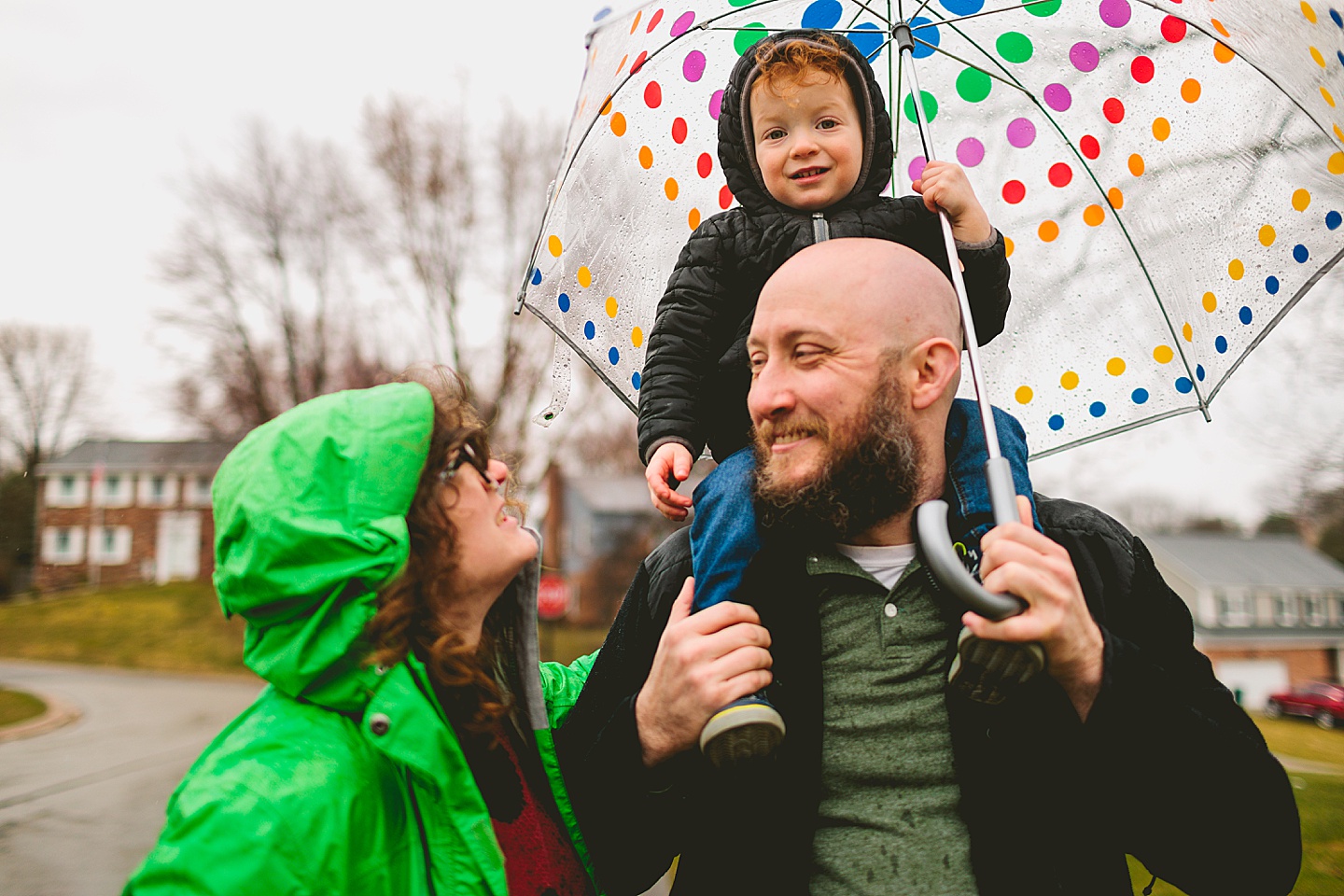 Parents taking a rainy day walk with toddler down the street