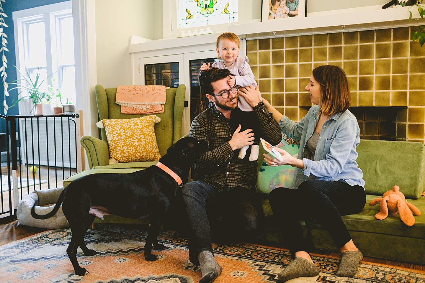 parents holding toddler in living room with black dog