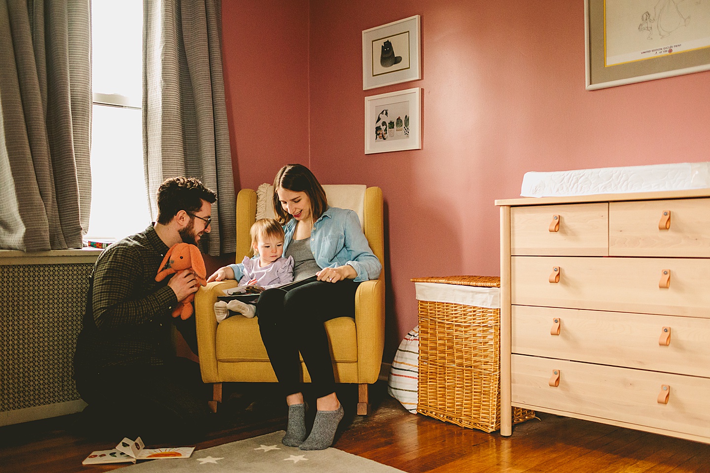 parents reading book to little girl in chair