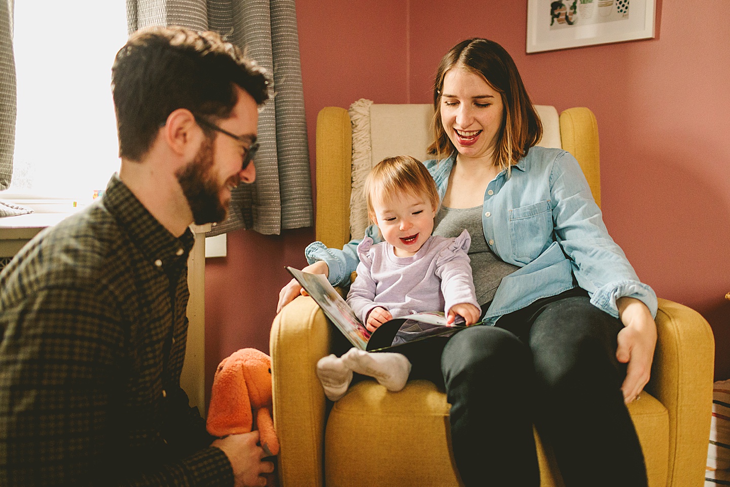 parents reading book to little girl in chair