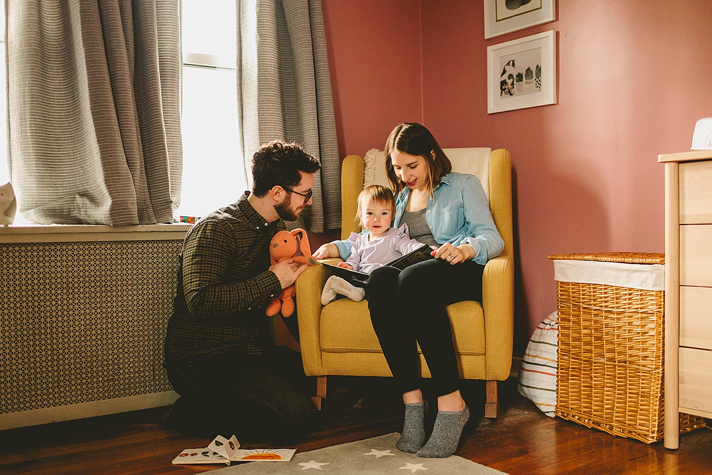 parents reading book to little girl in chair