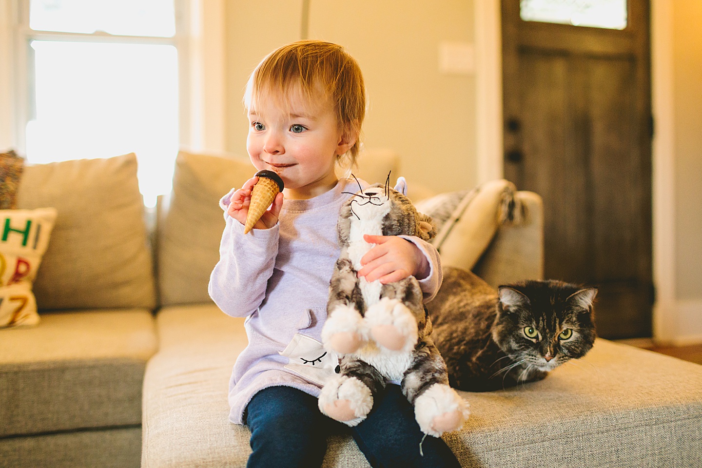 toddler eating ice cream next to cat while holding cat doll