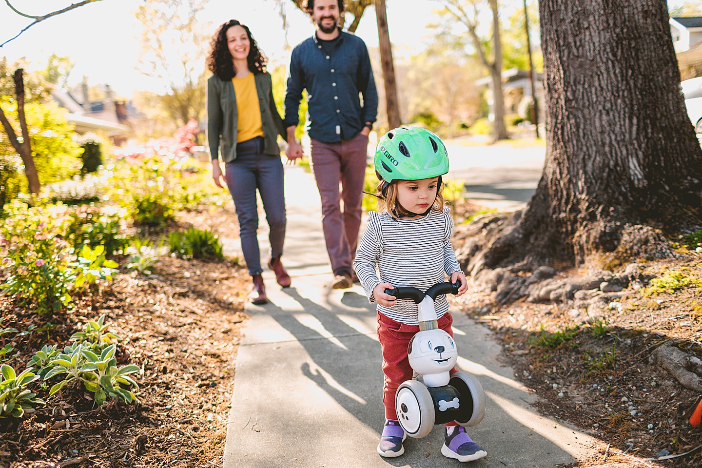 Girl walking her bike down the sidewalk with her mom and dad