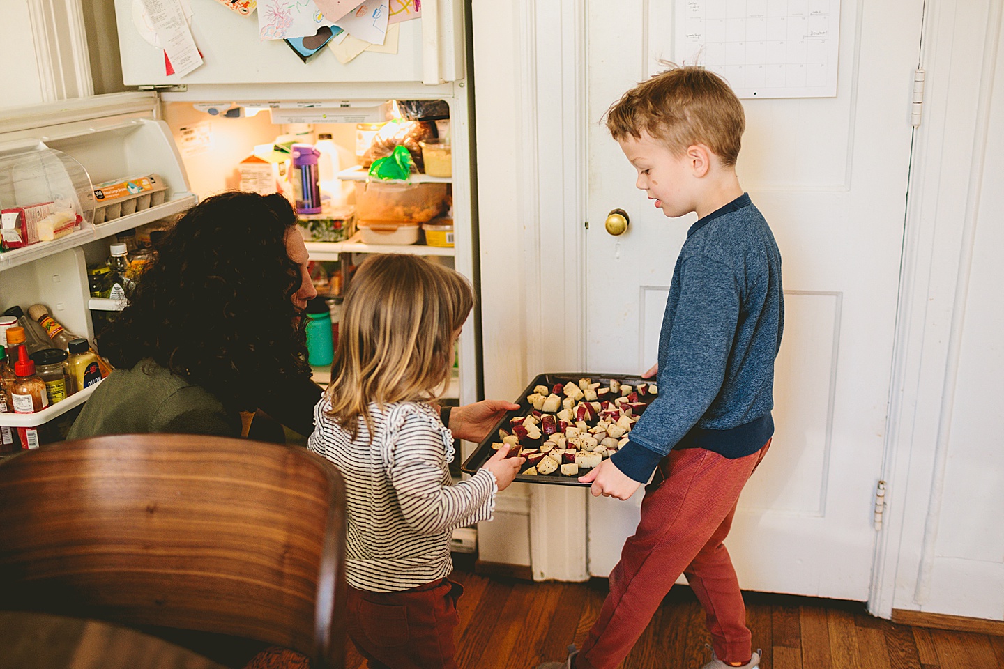 Kids carrying tray of potatoes through kitchen