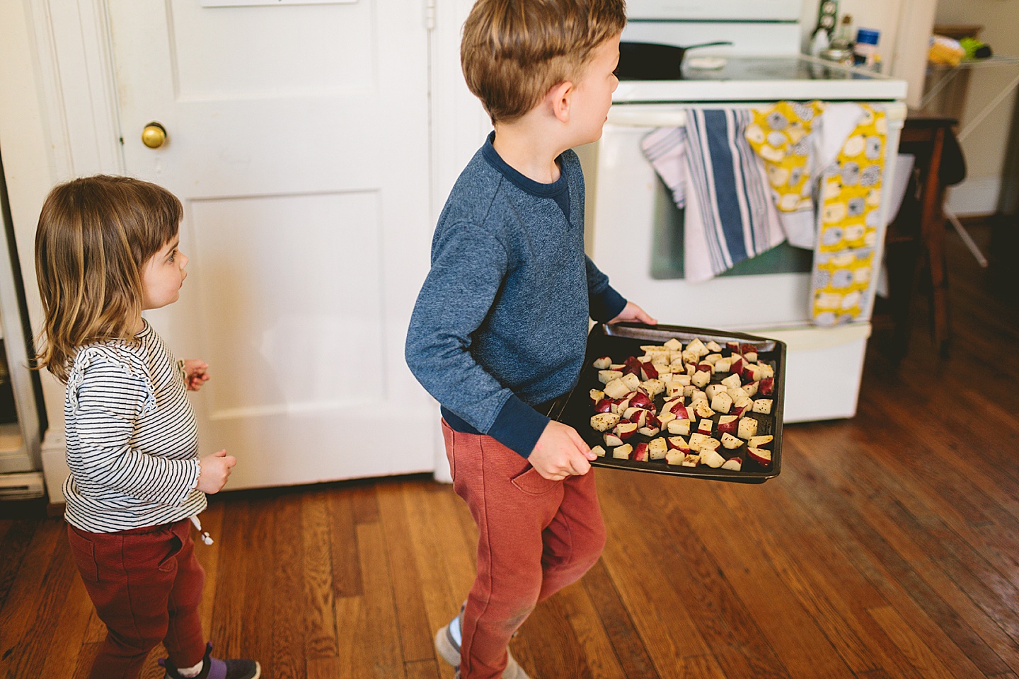 Boy carrying tray of potatoes through kitchen