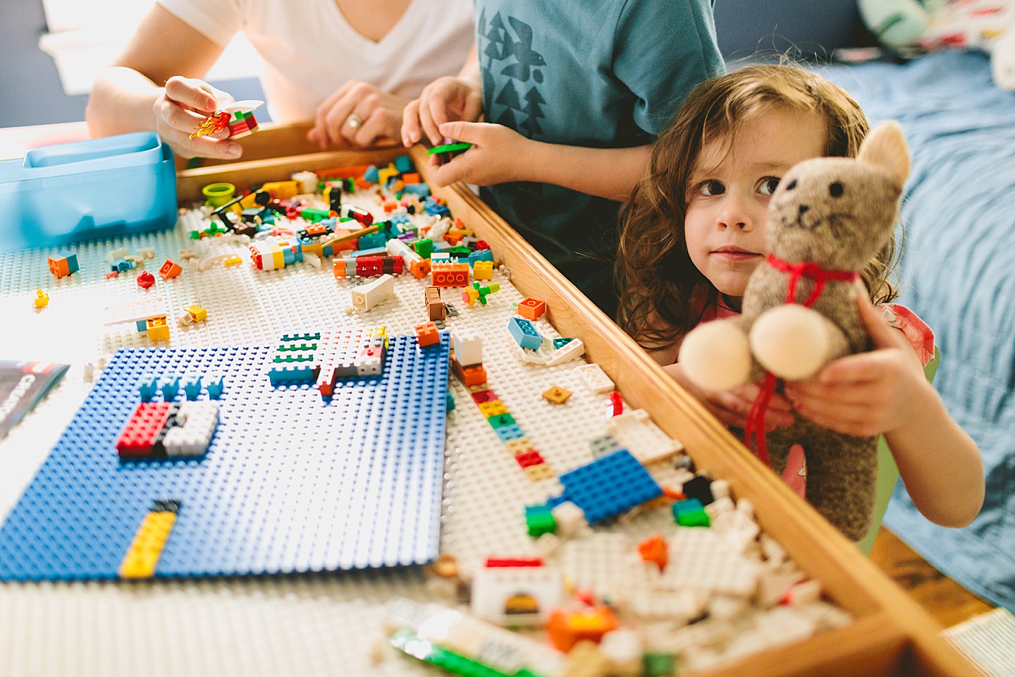 Girl holding up stuffed cat while building Legos