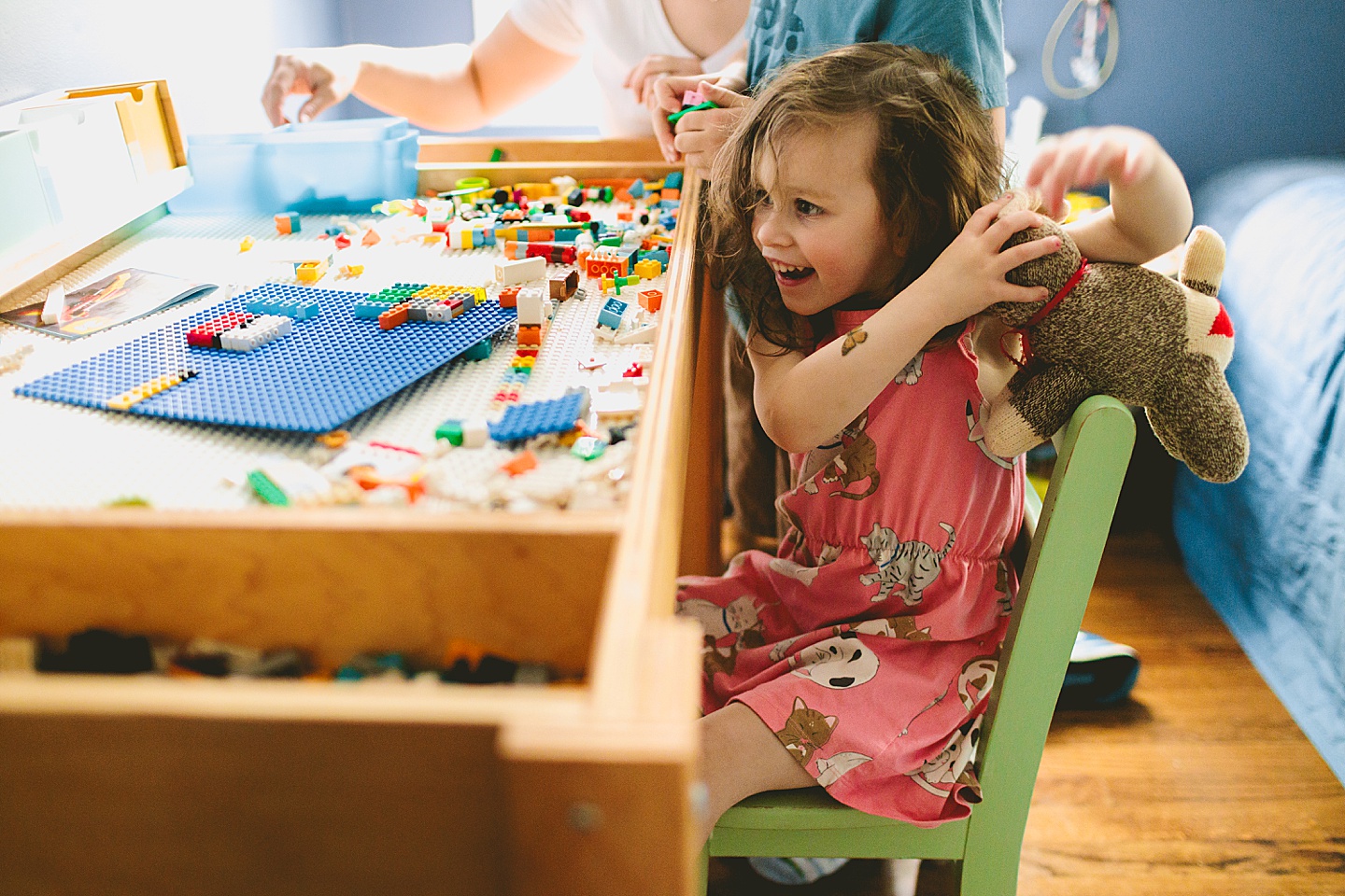 Girl holding up stuffed cat while building Legos