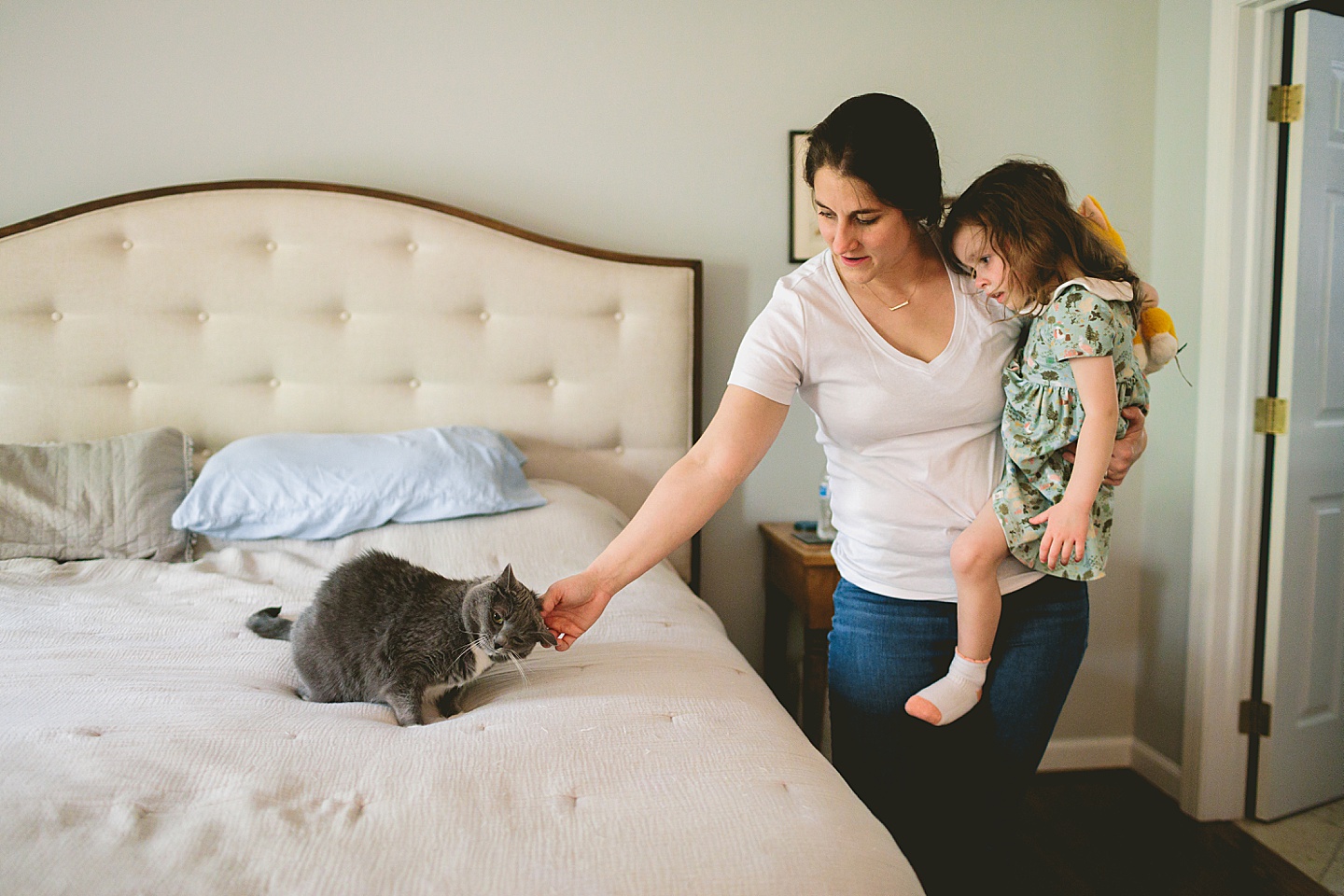 Mom holding daughter while petting cat on bed