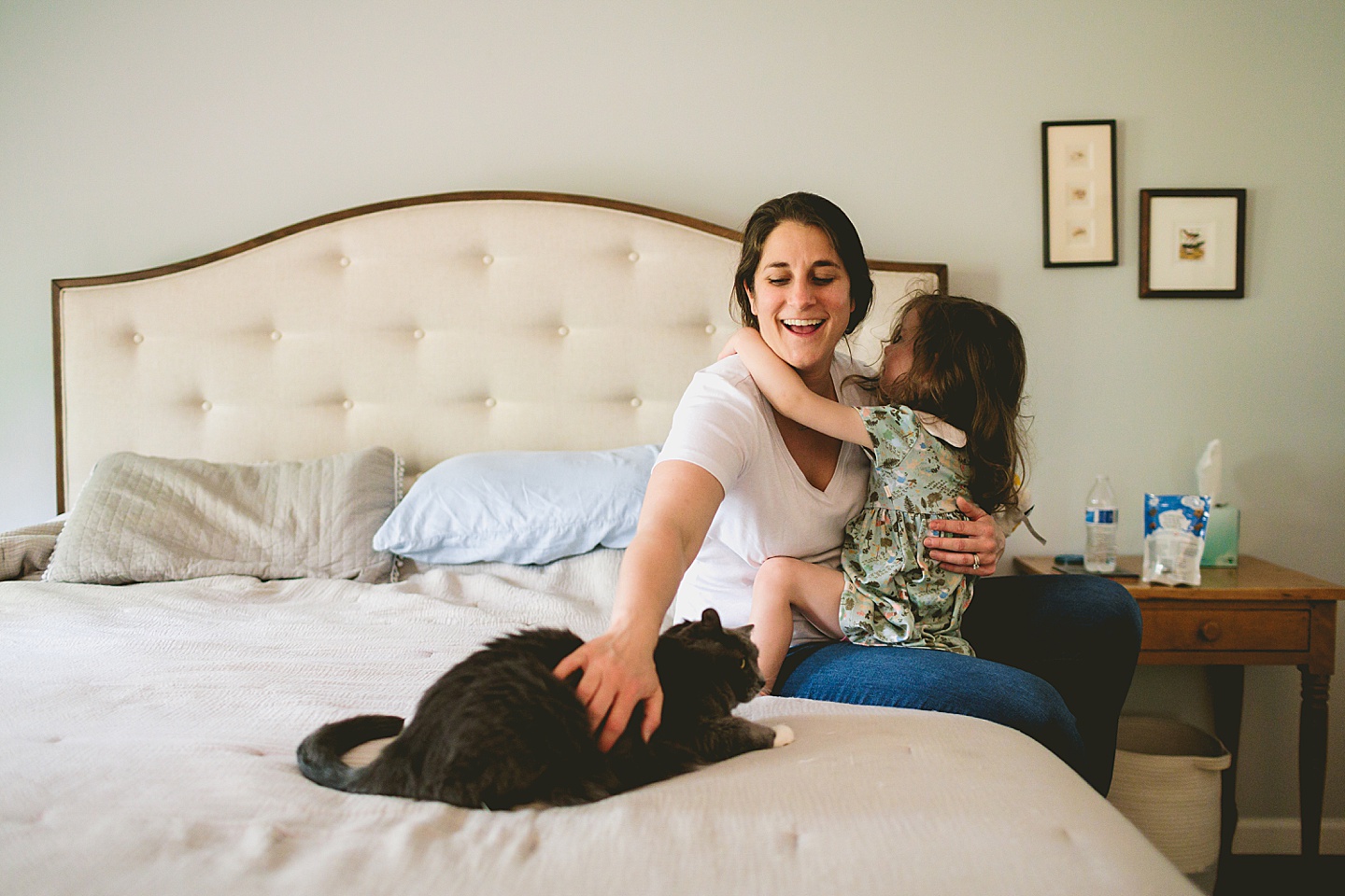 Mom holding daughter while petting cat on bed