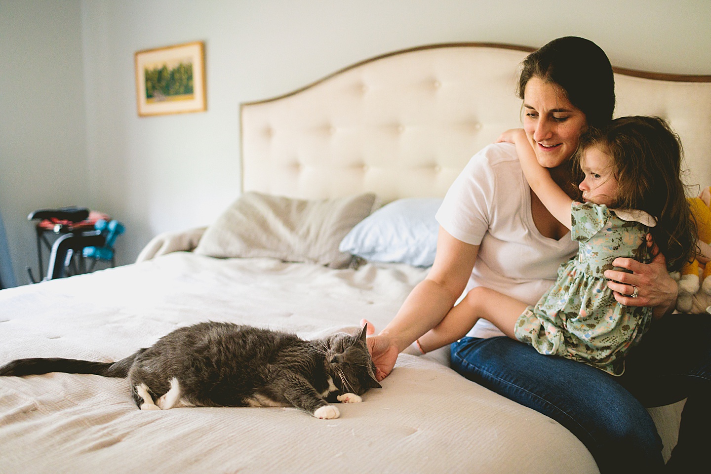 Mom holding daughter while petting cat on bed