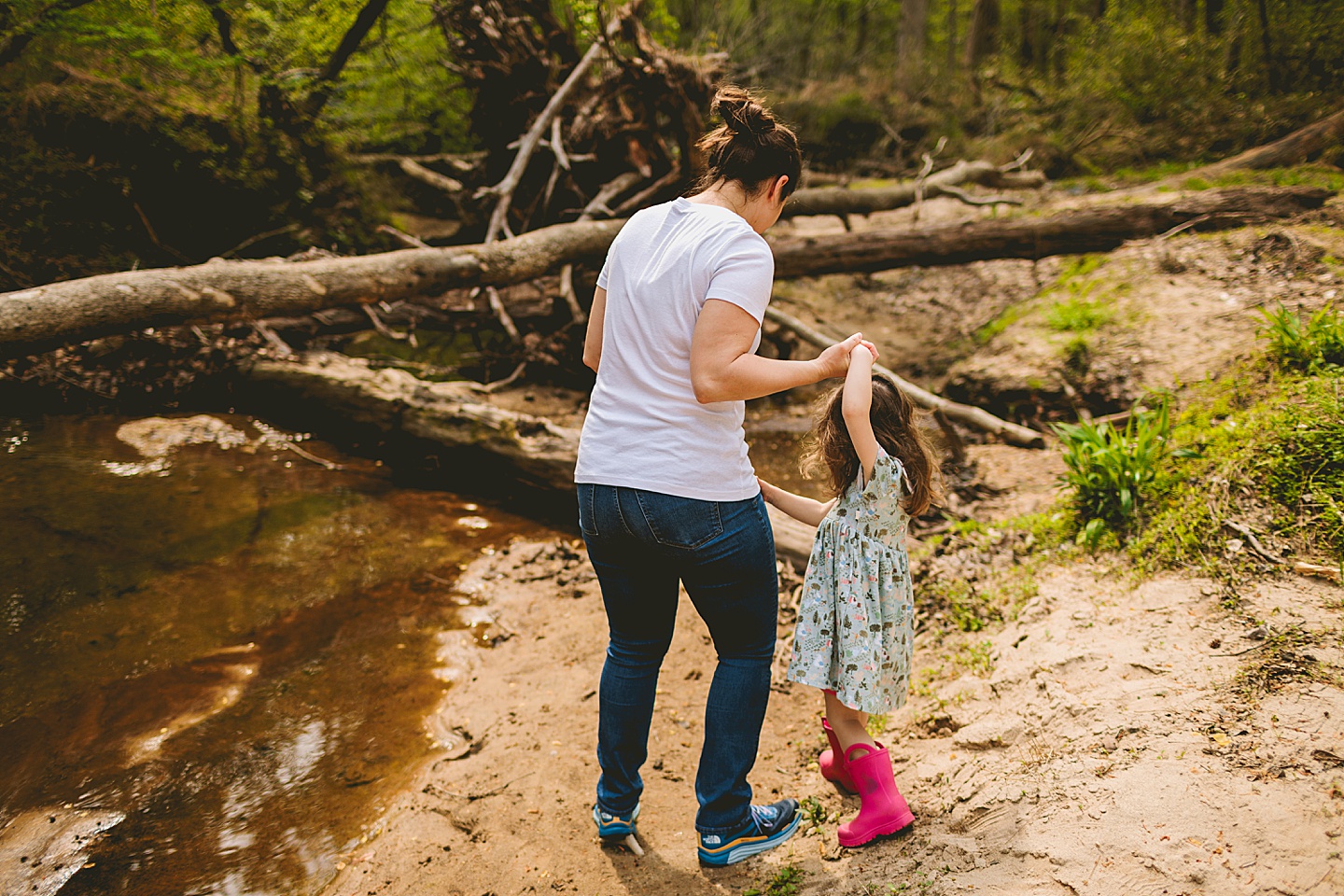 Mom walking daughter across a creek to a log