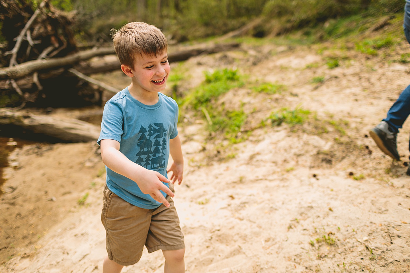 Boy laughing while playing in the sand on the side of a creek