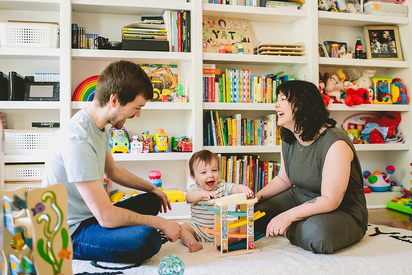 Baby sitting in front of library bookcase playing with toy cars with his mom and dad