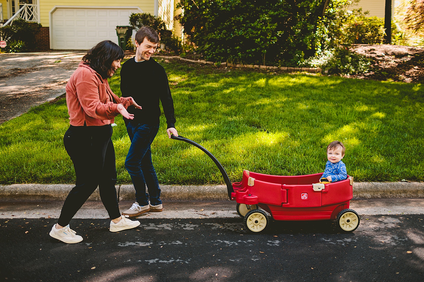 Parents pulling baby in red wagon down the street