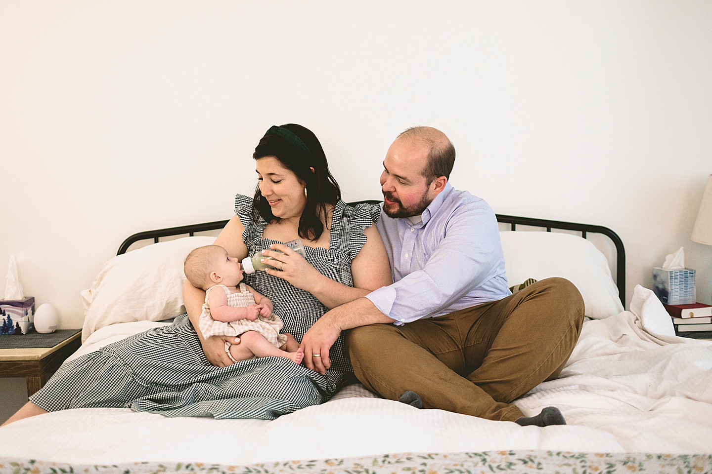 Mom feeding baby a bottle while sitting on bed 