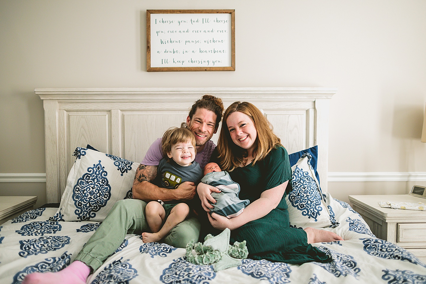 Family sitting together and smiling on bed for family photos in Raleigh