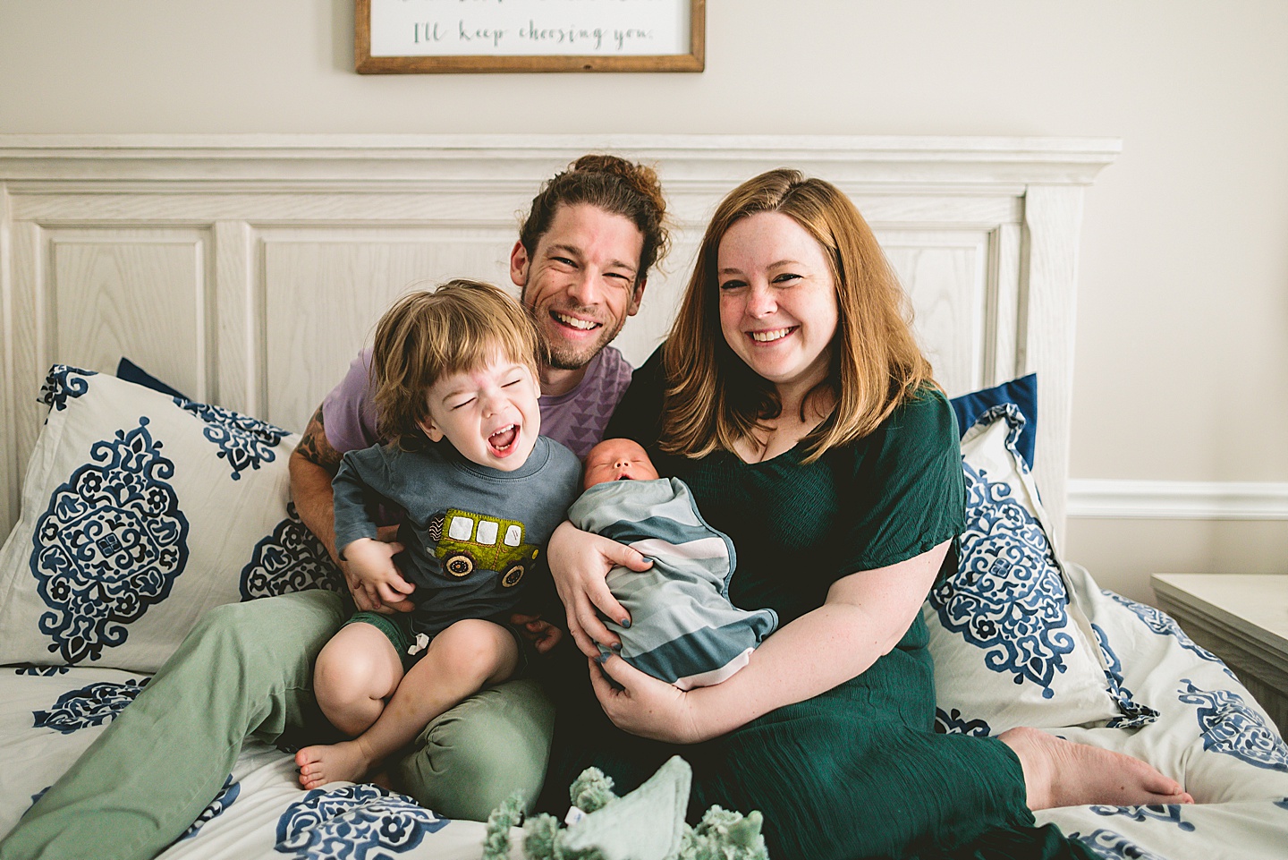 Family sitting together and smiling on bed for family photos in Raleigh