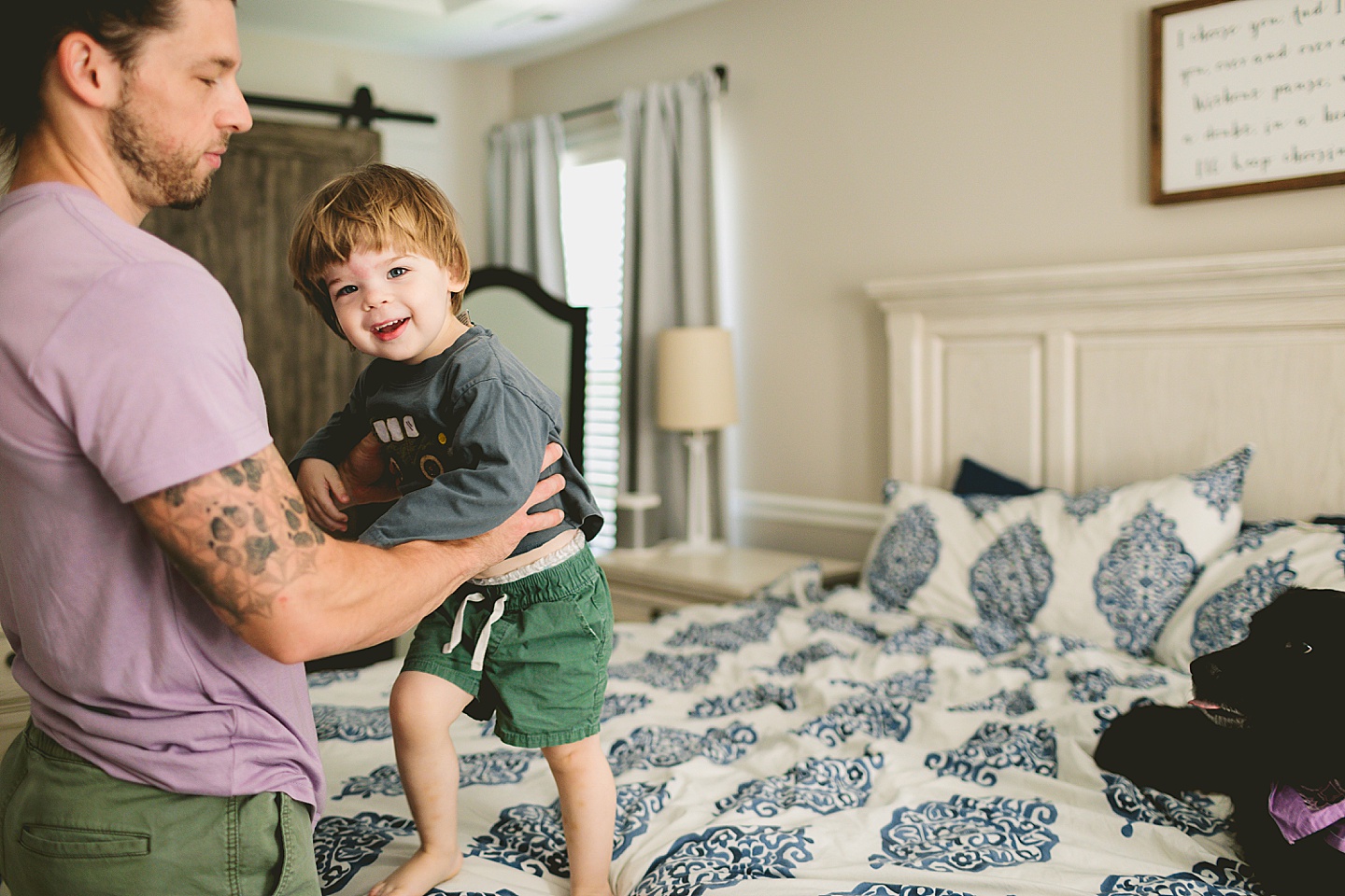 Toddler jumping on the bed with black dog