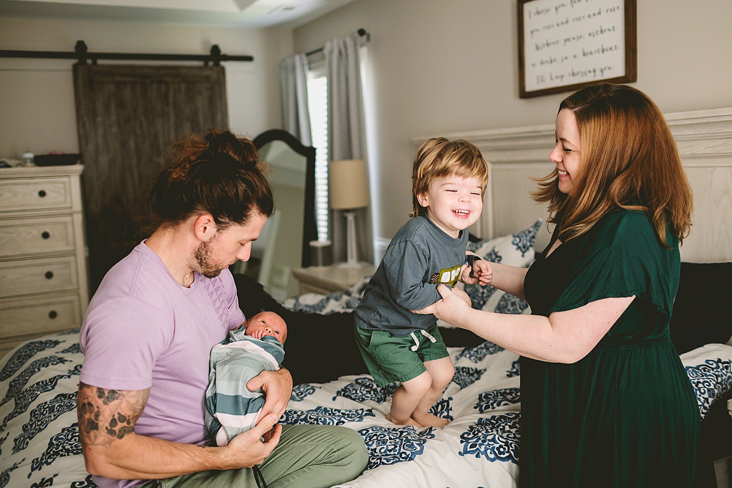 Mom helping toddler jump on the bed while Dad sits and holds baby