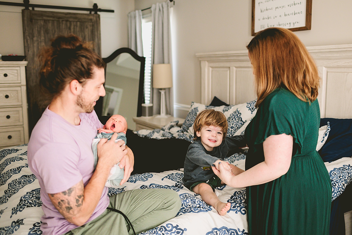 Mom helping toddler jump on the bed while Dad sits and holds baby