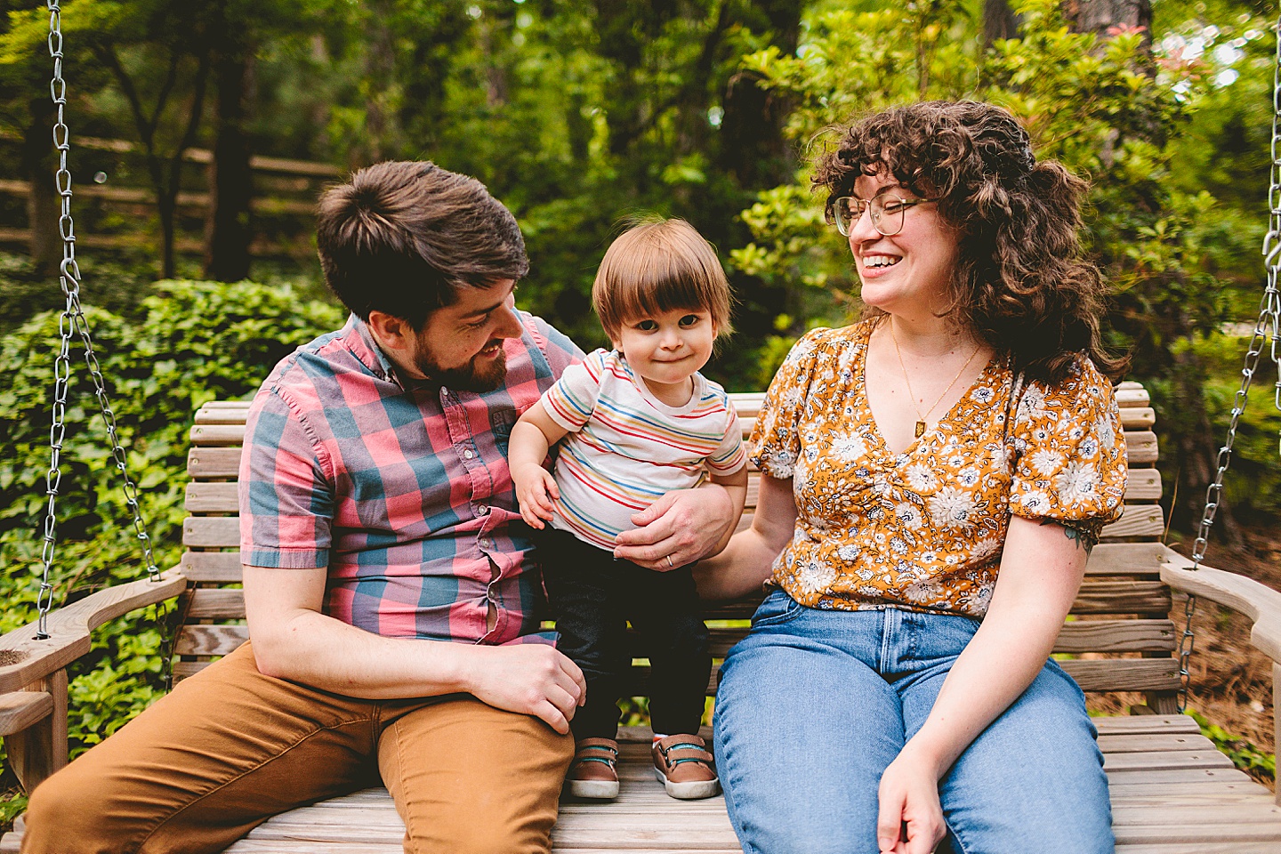 Toddler standing with parents on swing