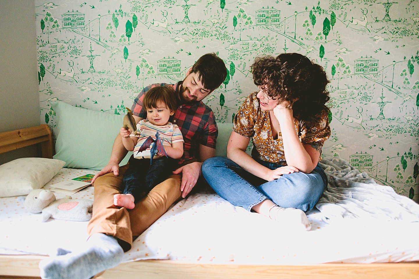 Parents reading a book to a toddler in front of wallpaper during family photographs in Durham NC