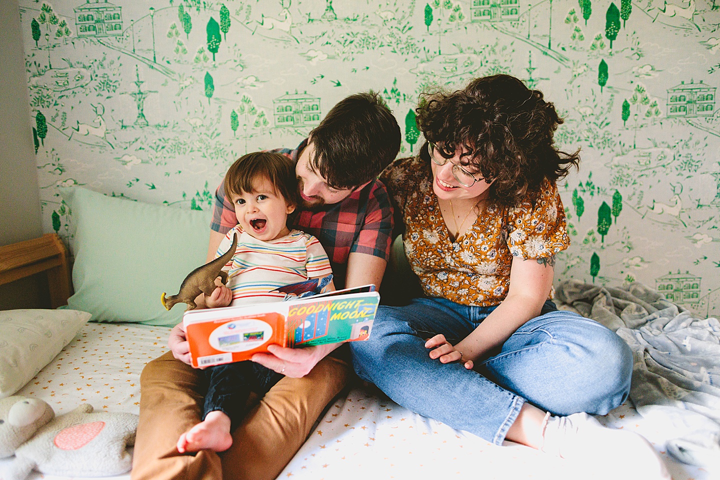 Parents reading a book to a toddler in front of wallpaper during family photographs in Durham NC