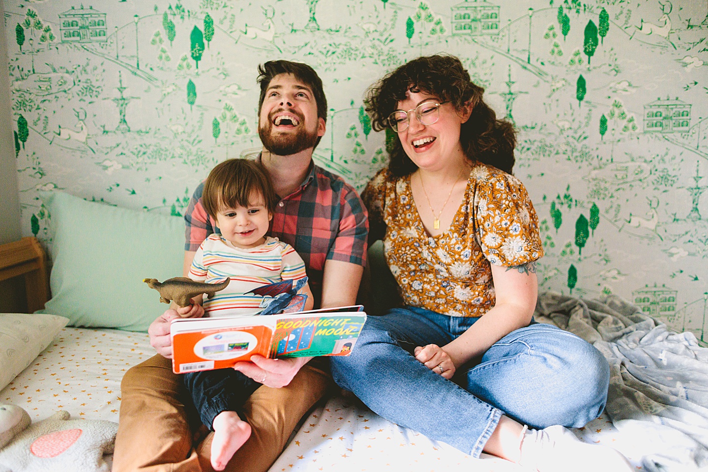 Parents reading a book to a toddler in front of wallpaper during family photographs in Durham NC