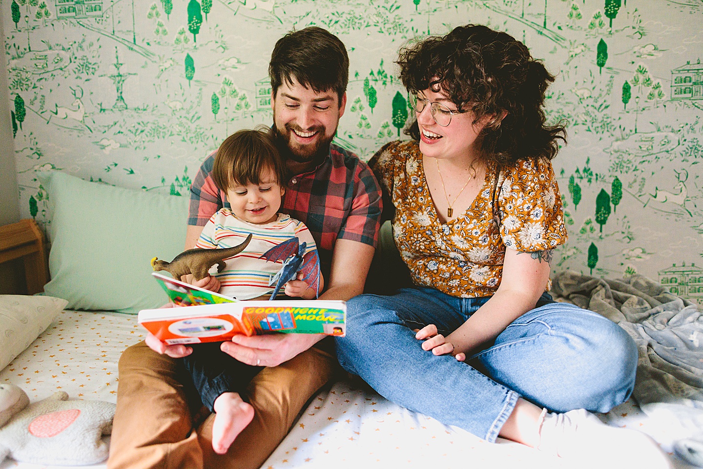 Parents reading a book to a toddler in front of wallpaper during family photographs in Durham NC