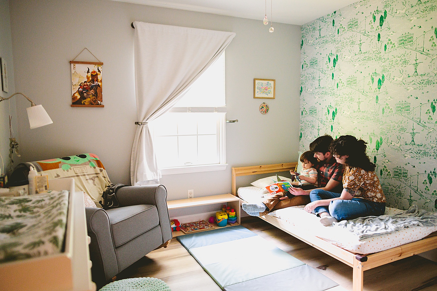 Parents reading a book to a toddler in front of wallpaper during family photographs in Durham NC