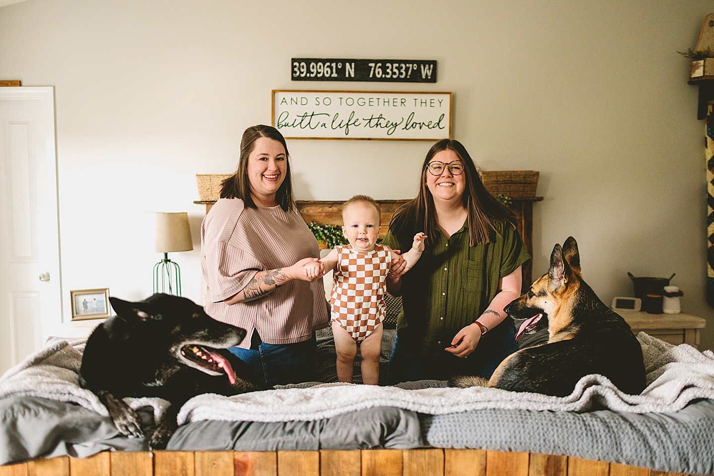 Moms holding baby's hand on a bed with two dogs