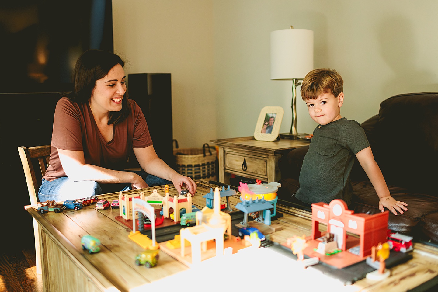 Kid playing with set of cars in the living room with his mom