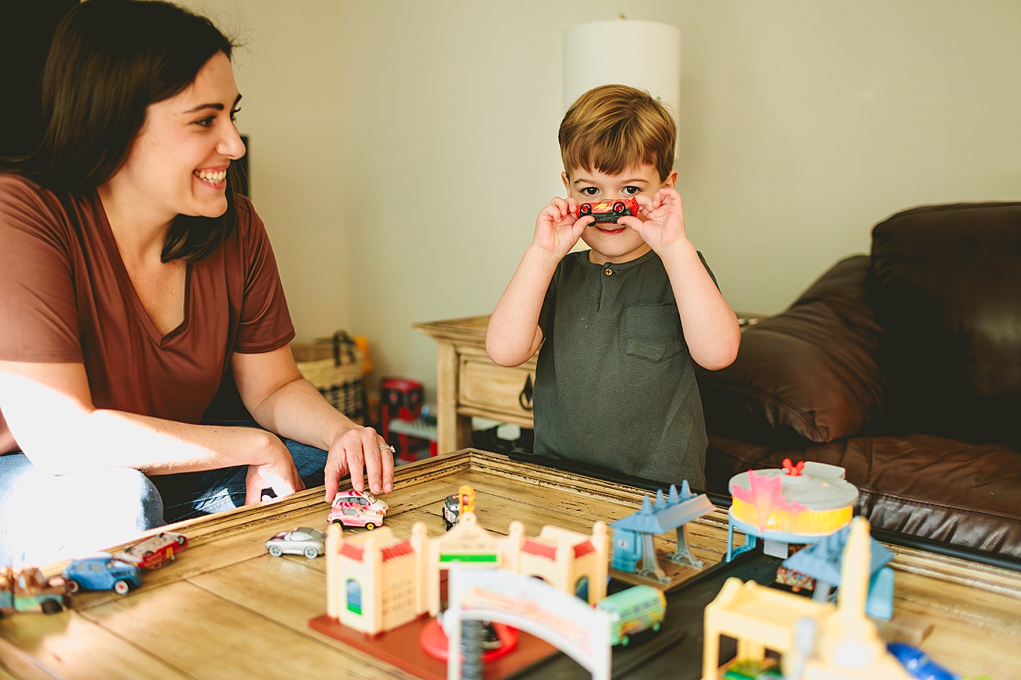 Kid playing with set of cars in the living room with his mom