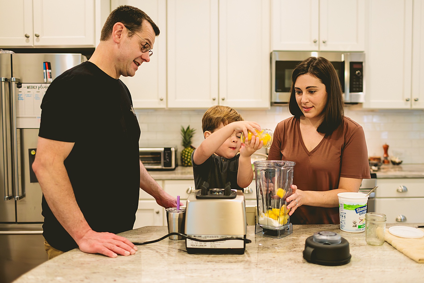 Kid making a smoothie with his parents in the kitchen