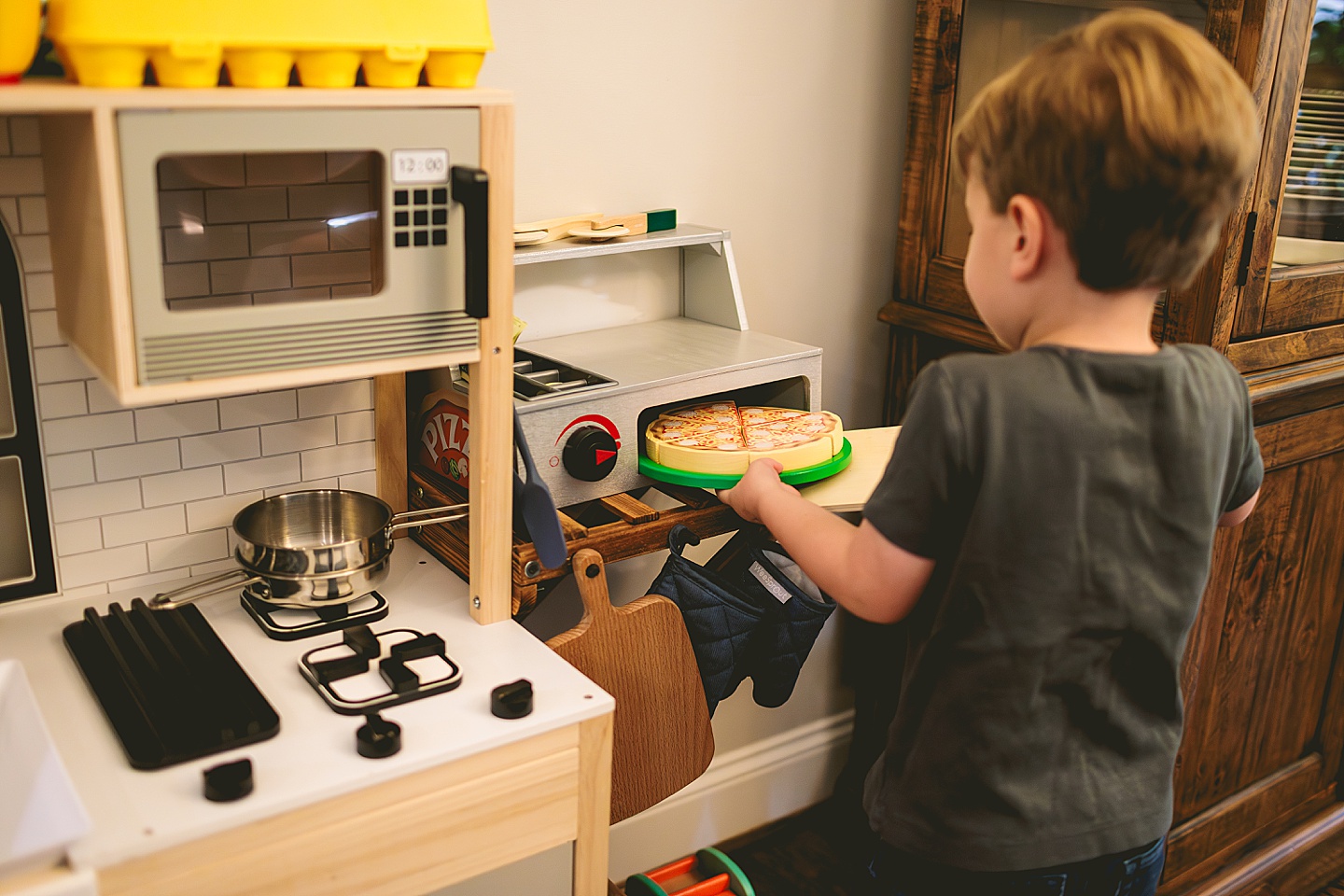Toddler using play kitchen to make pizza for his family