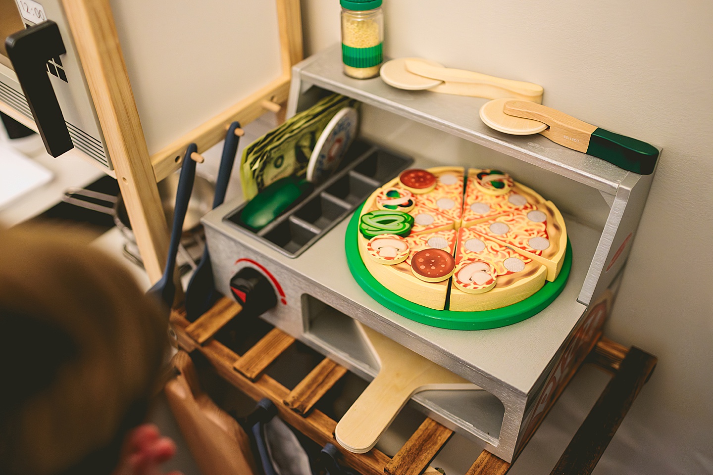 Toddler using play kitchen to make pizza for his family