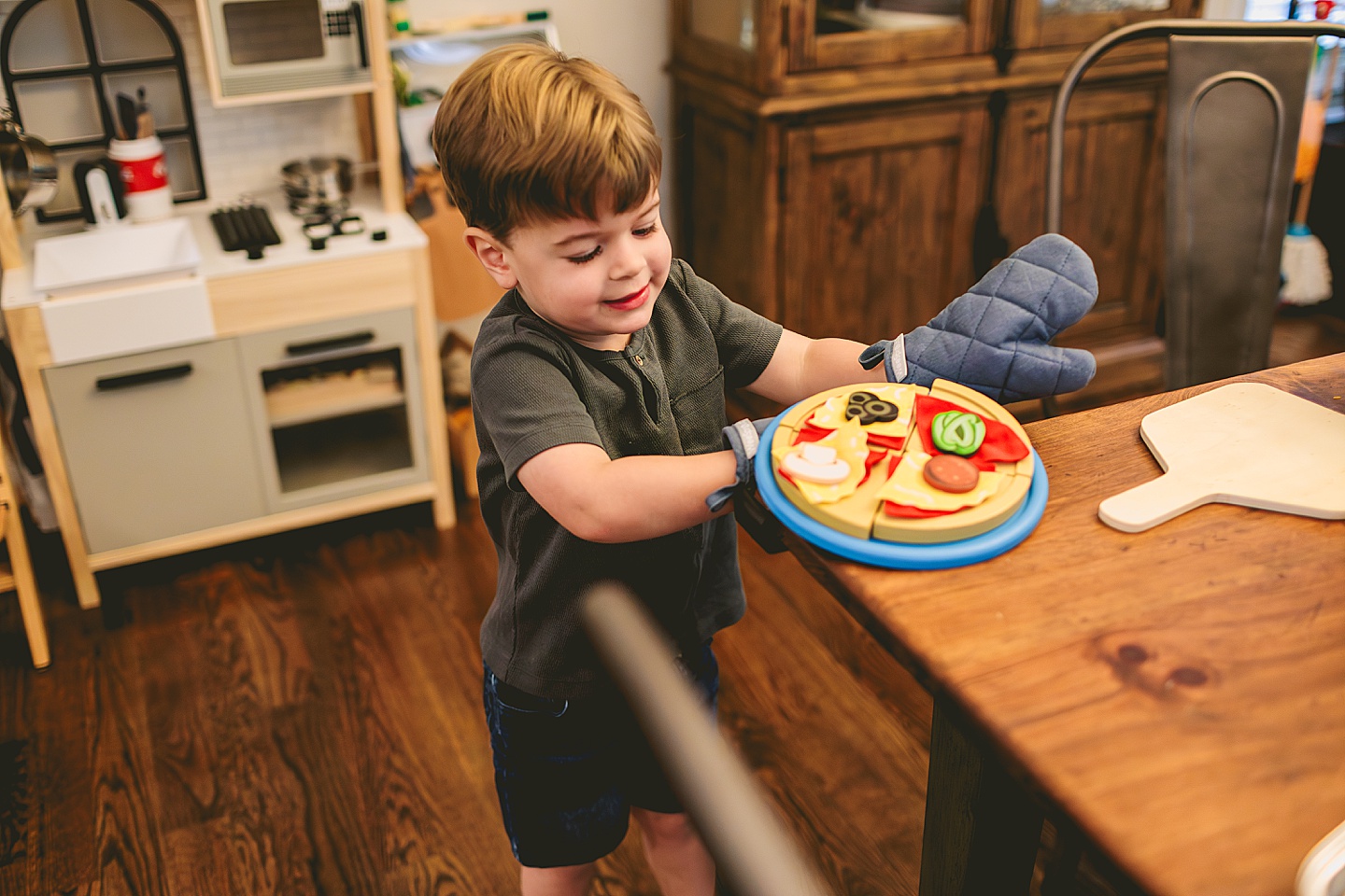 Toddler using play kitchen to make pizza for his family
