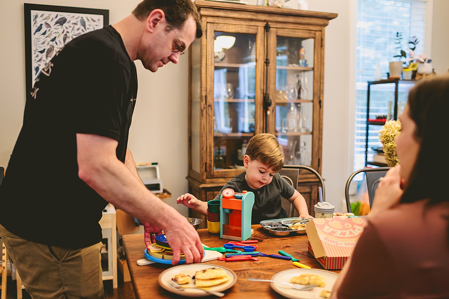 Toddler using play kitchen to make pizza for his family