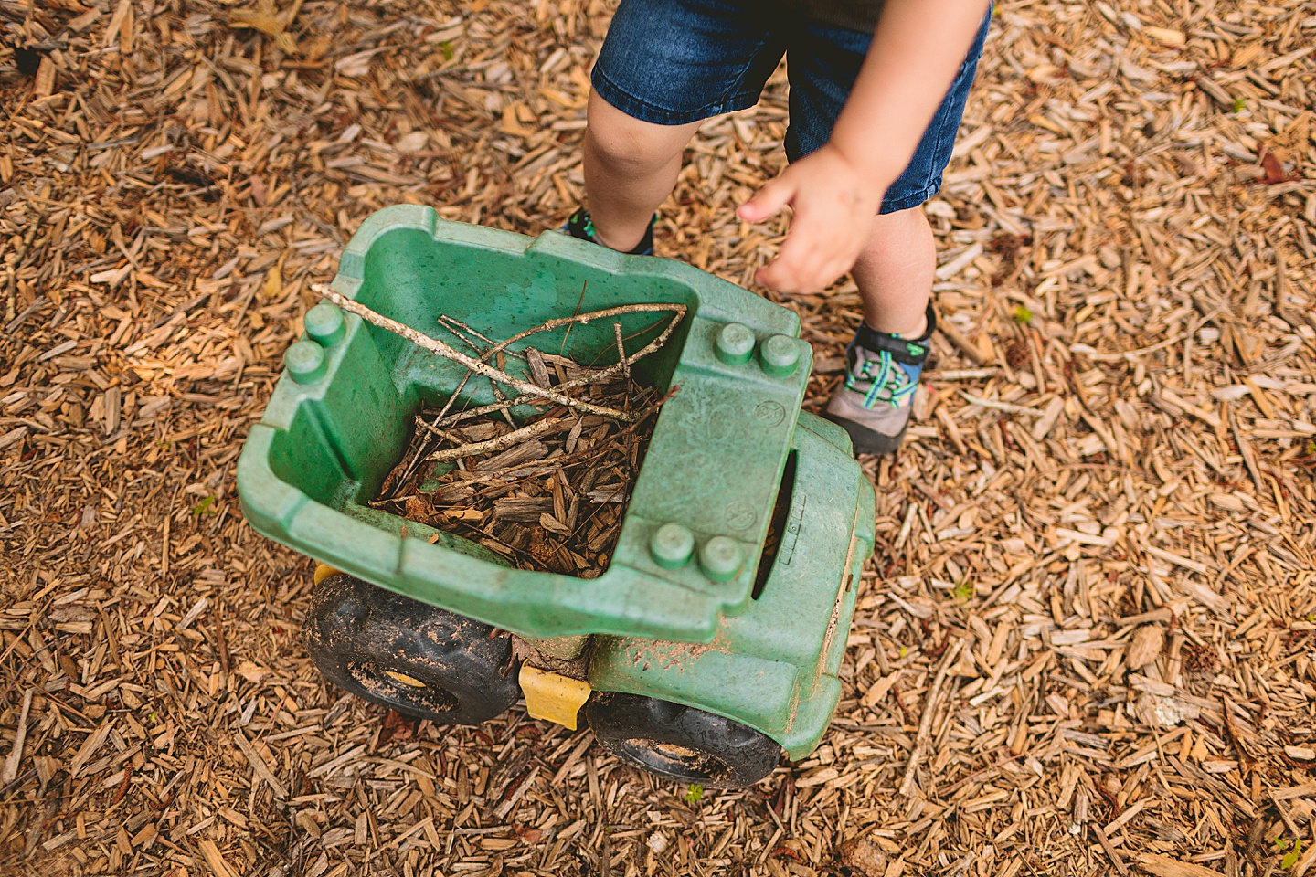 Kid filling dump truck with sticks and mulch