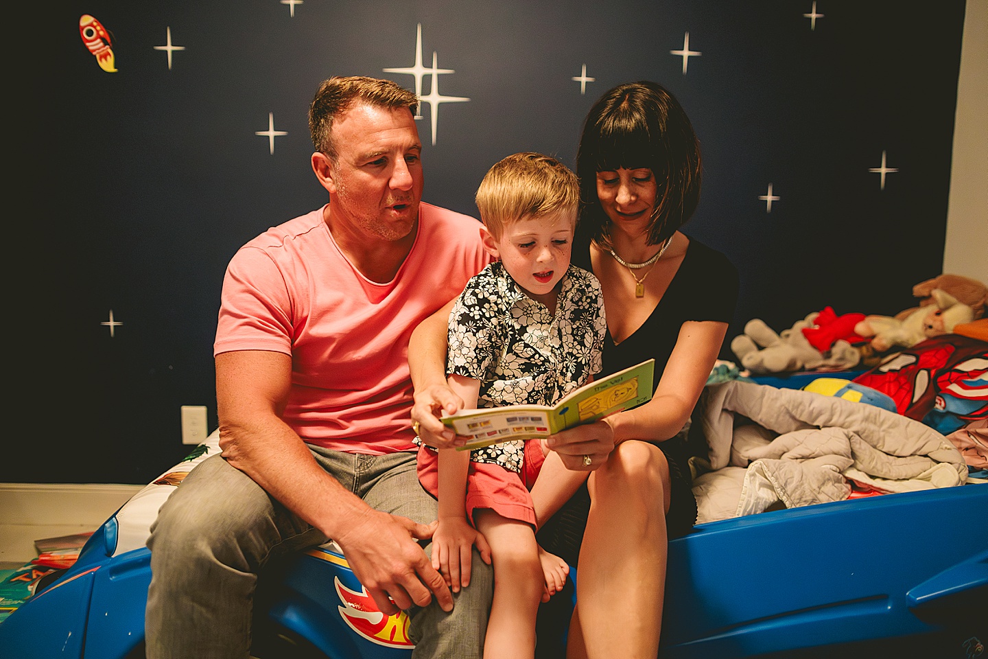 Boy sitting on bed with his parents reading a book