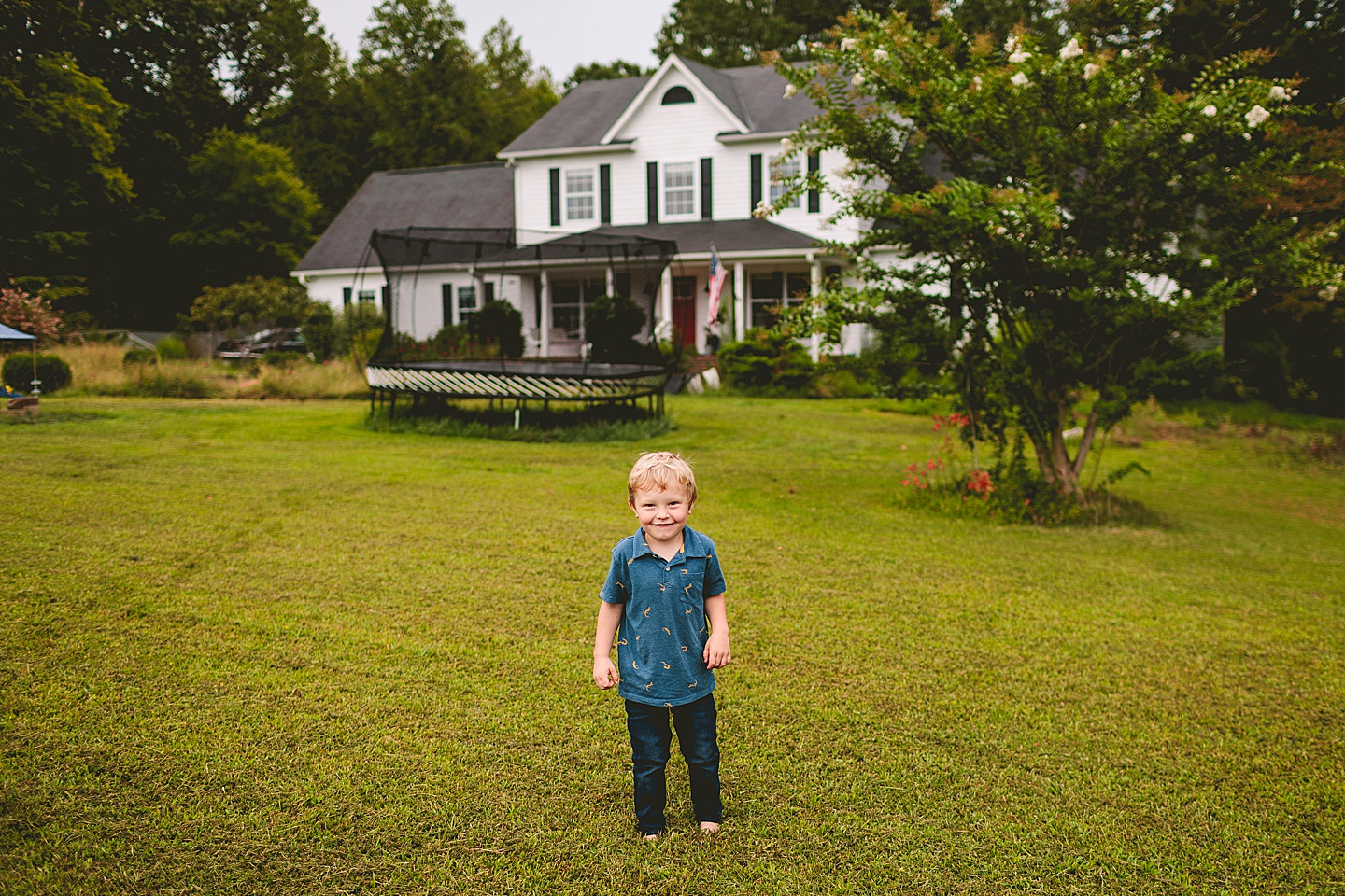 Kid standing in front of his house with trampoline in the background
