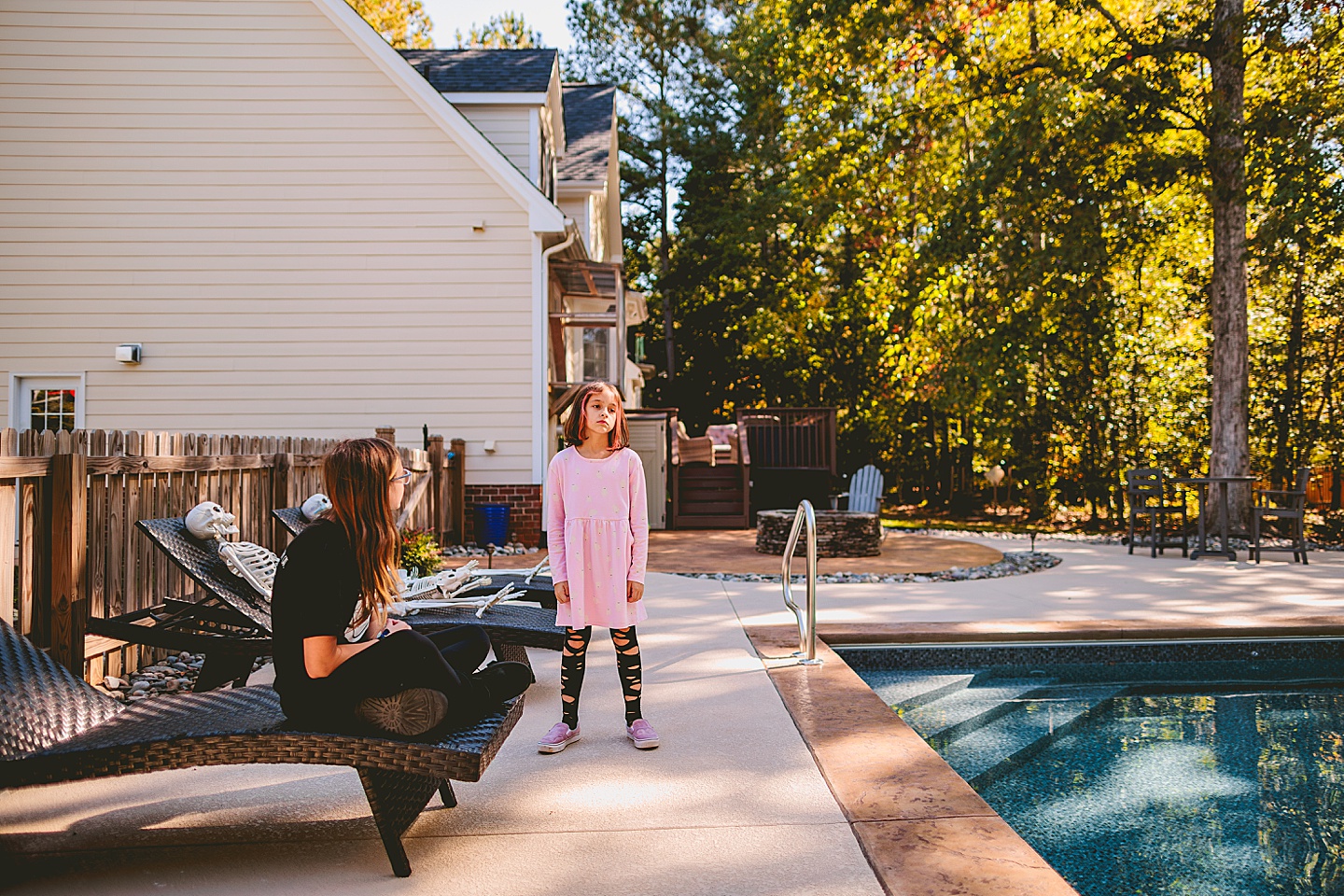 Two sisters hang out by the side of a swimming pool in fall