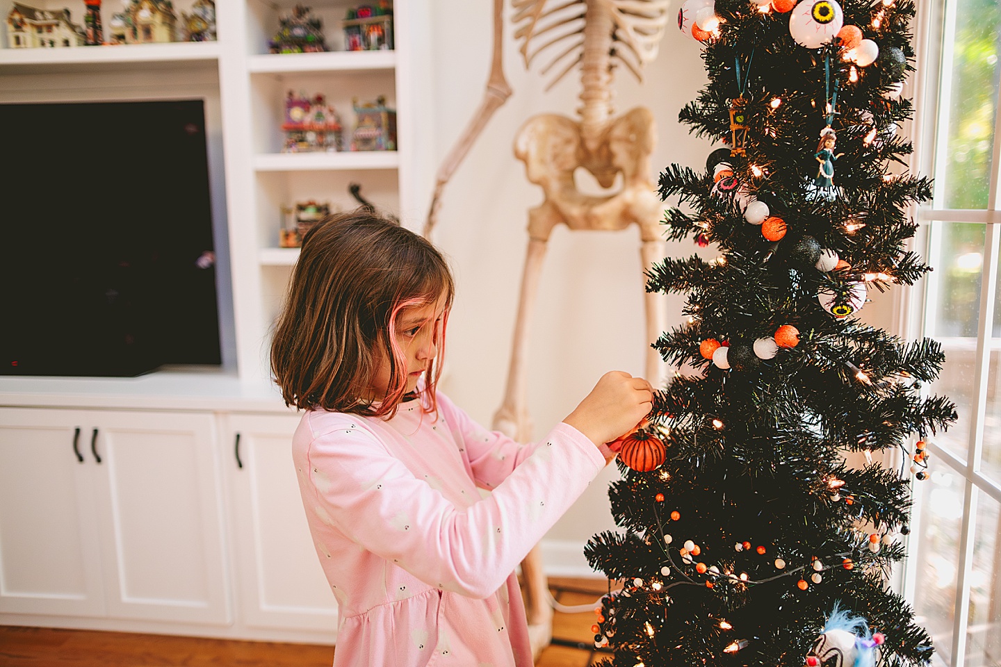 Girl hangs pumpkin ornament on a black Halloween tree
