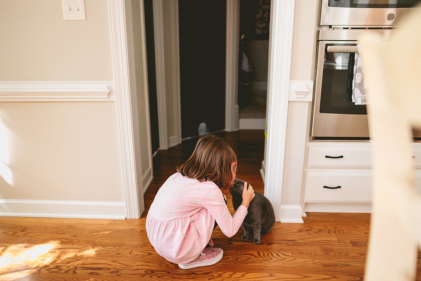 Girl crouched down on the kitchen floor giving gray cat a kiss on the head