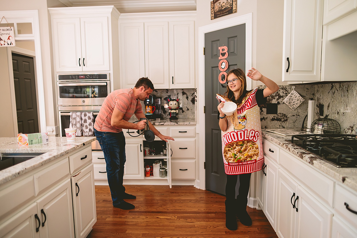 Dad puts away something in a kitchen cabinet while daughter prepares Cup o Noodles soup